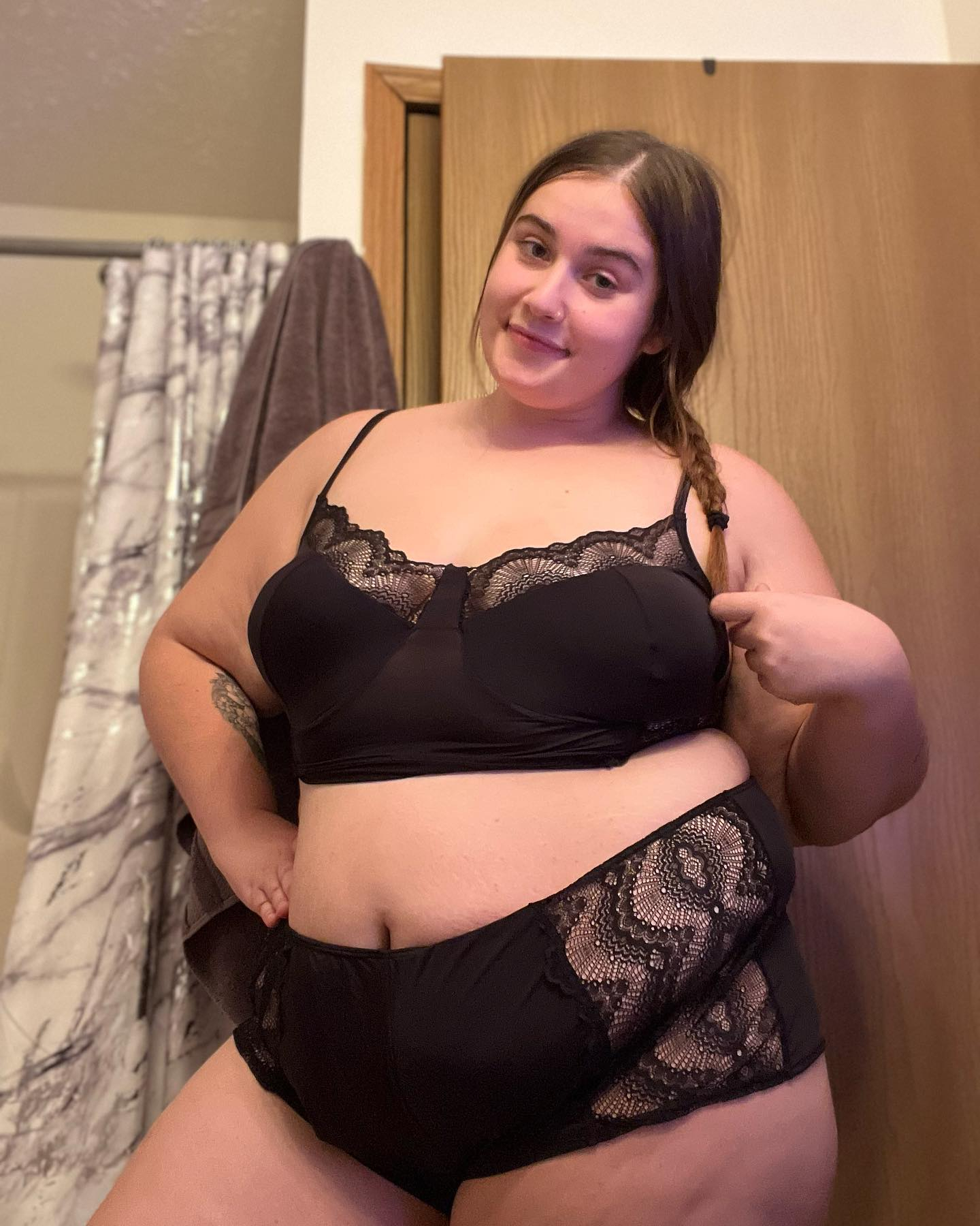 Woman in black lace lingerie smiling softly in a bathroom.