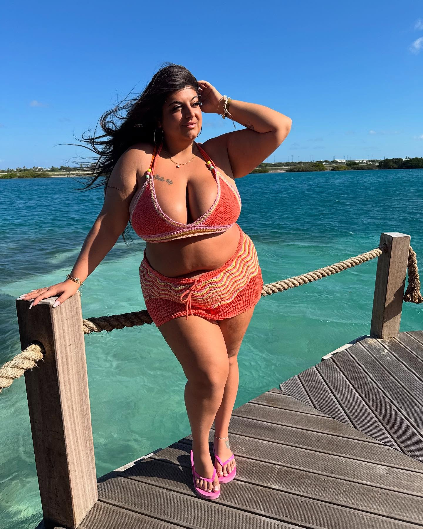 Woman in a coral crochet bikini set posing on a pier by blue water.