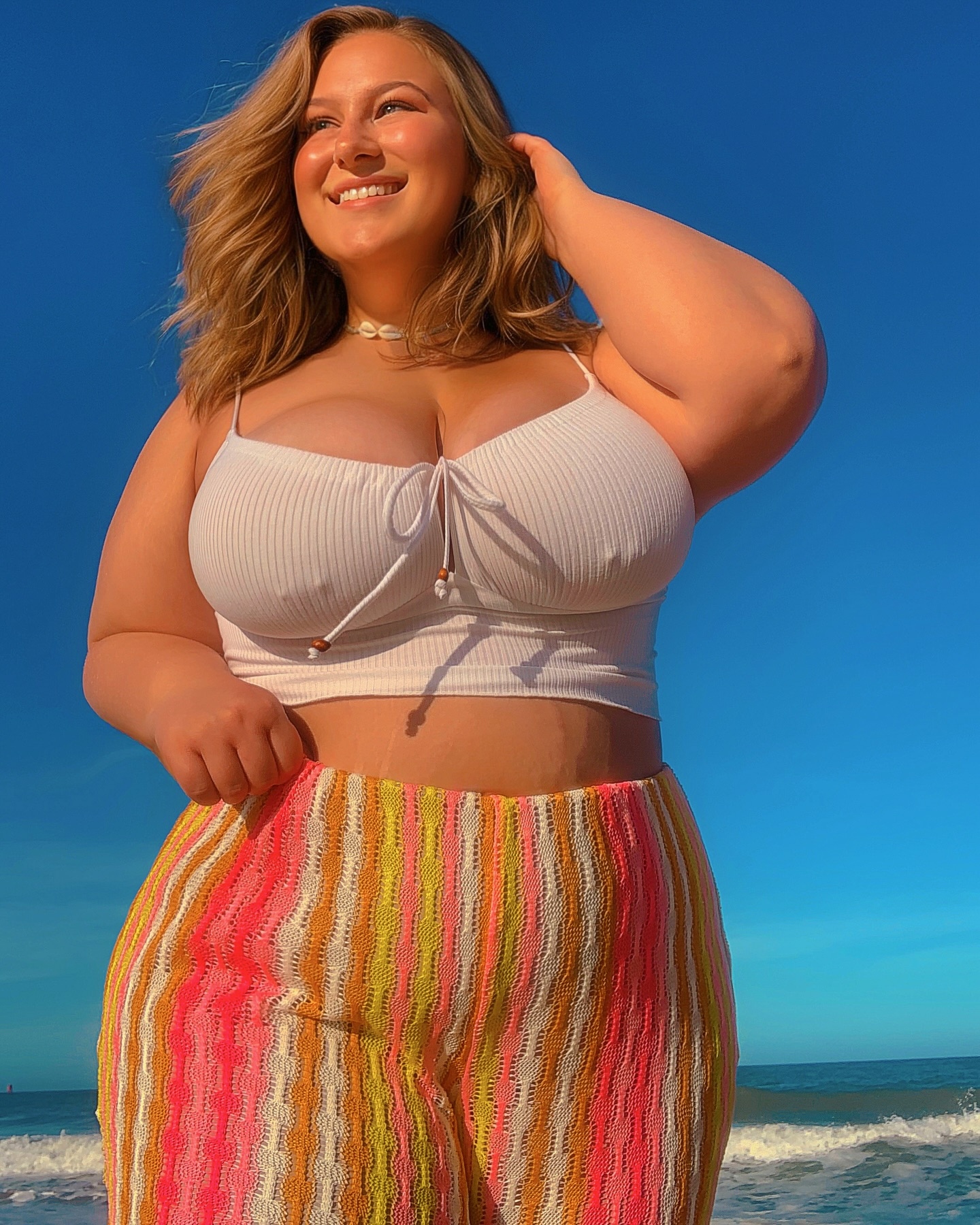Woman in crop top and striped pants on beach.