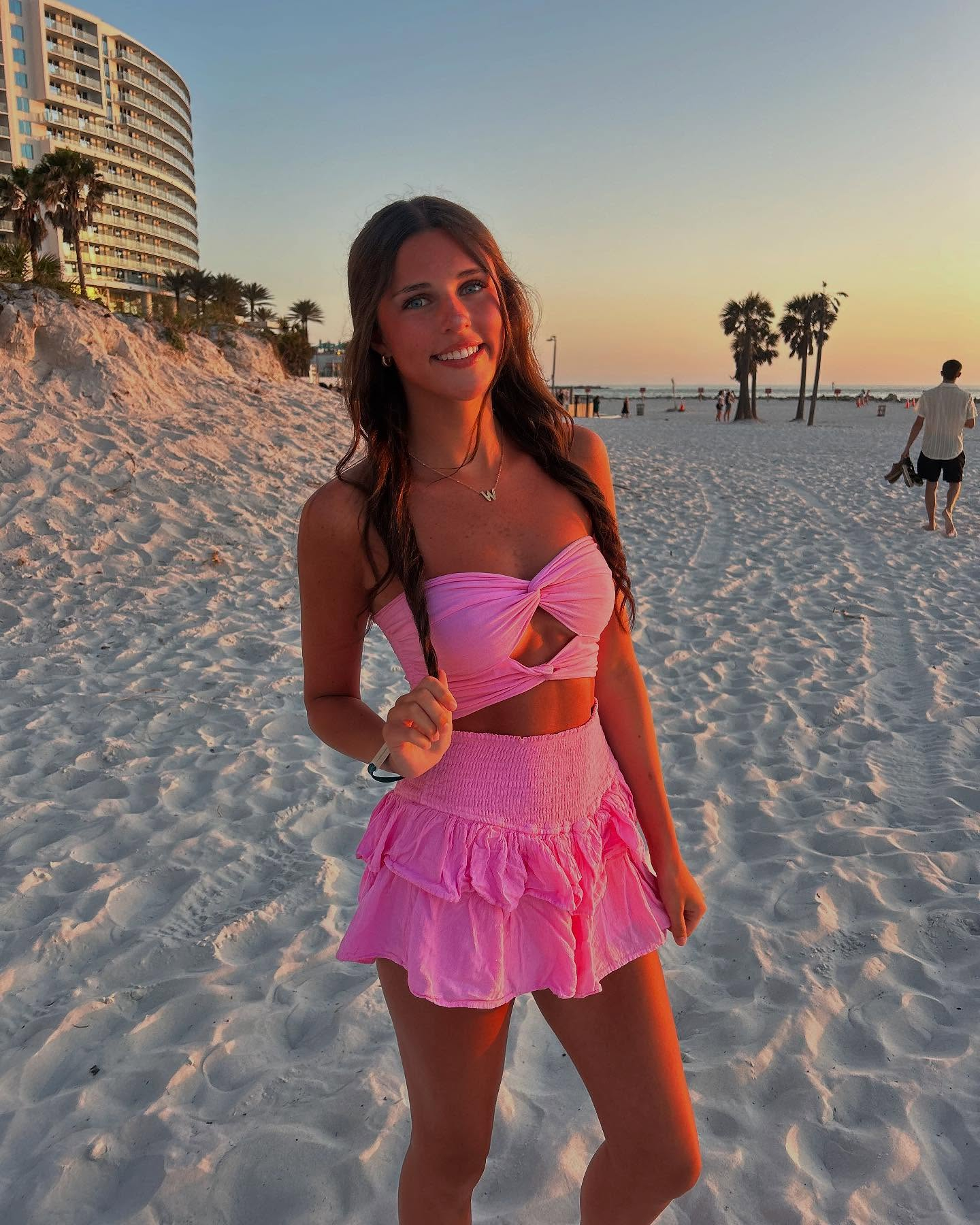 Woman in pink outfit on beach at sunset.