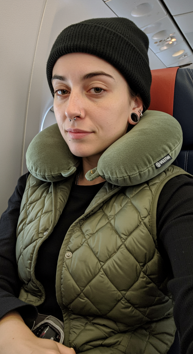 Person wearing a beanie, quilted vest, and neck pillow on an airplane.